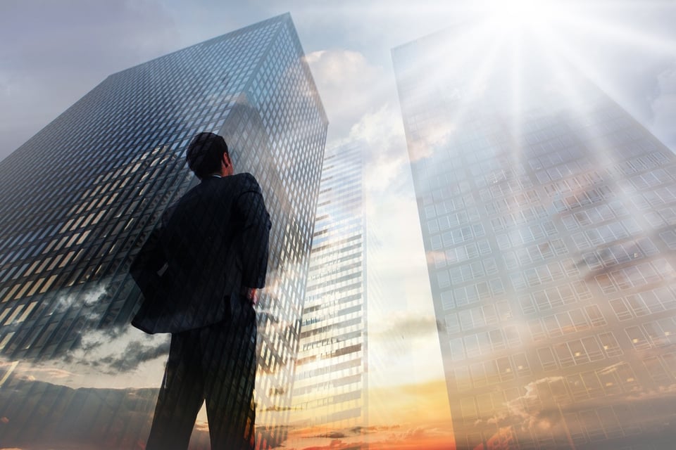 Businessman standing with hands on hips against low angle view of skyscrapers at sunset.jpeg